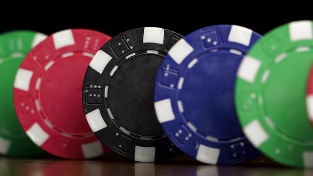 Poker chips stand in a row on a black background, a Domino effect. Playing poker chips are on the table, a symbol of casino