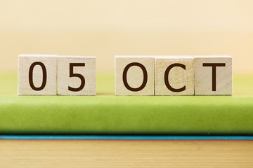 Wooden cube shape calendar for OCT 5 on green book, table.  