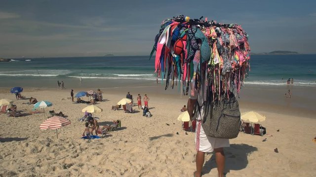 a man carries a rack of bikinis on his head at ipanema in rio de janeiro, brazil