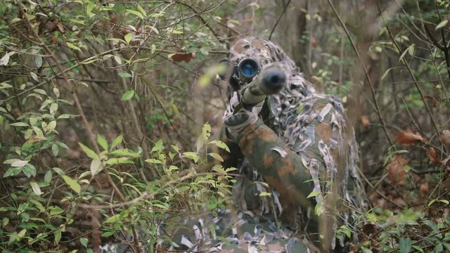 Armed young soldier sniper in a zone of armed conflict in uniform in forest, slow motion. Airsoft
