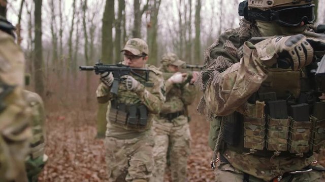 Group of armed young soldiers in a zone of armed conflict in uniform targeting with assault rifles in forest, slow motion, airsoft