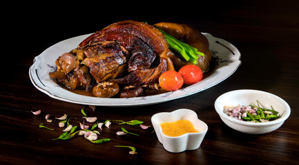 Stewed pork leg in white dish on wooden background with dim light. Asia food / Still Life