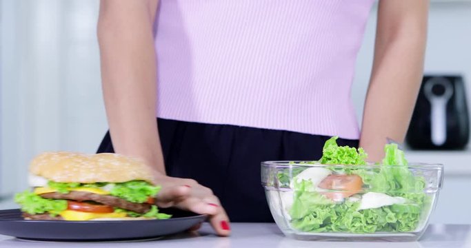 Dieting concept. Close up of anonymous woman hands choosing a bowl of salad and refuse a plate of burger. Shot in 4k resolution