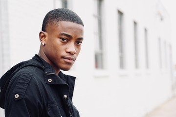 Portrait of a young African American male model against a white building background with copy space