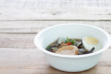 Clear Kuayjub Soup on wooden table food of Thailand.In the cup consist of noodles, pork, liver, eggs, crabs.