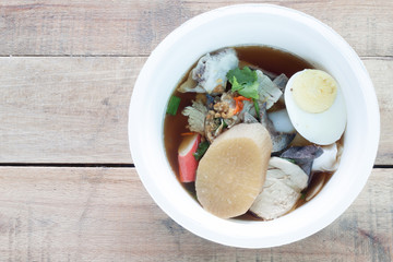 Clear Kuayjub Soup on wooden table food of Thailand.In the cup consist of noodles, pork, liver, eggs, crabs.