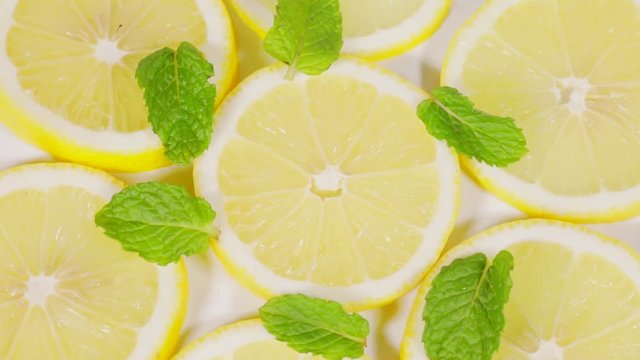 Video footage of slices of lemon fruits and peppermint leaves spinning on the table