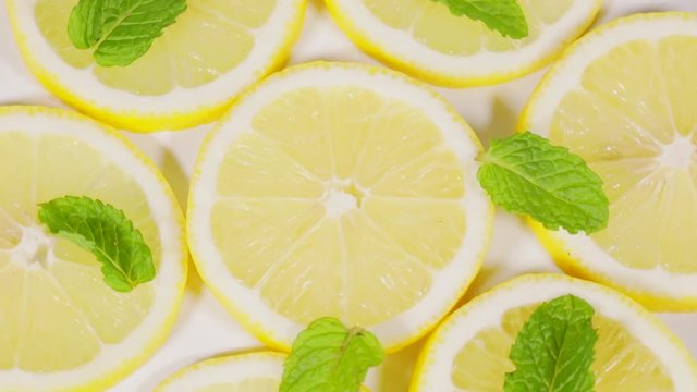 Close up of slices of juicy lemon fruits and peppermint leaves spinning on the table in the studio