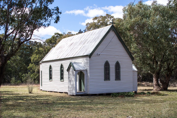 Fototapeta na wymiar White wooden rural country church with arched windows set against bushland background