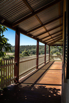Outdoor verandah patio deck of sandstone brick cottage with picket fence in sunshine with trees in background