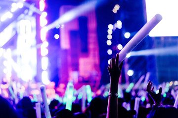 Fototapeta na wymiar Crowd of hands up glow stick concert stage lights and people fan audience silhouette raising hands in the music festival rear view with spotlight glowing effect