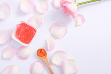 Spa accessories in Pink. Top view of body cream and pink rose flower petals on white background.