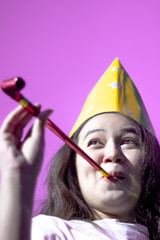 Attractive young women wearing party hat cheering and celebrating blowing party horn. Funny lovely girl blowing in party whistle and copy space over pink background. New year and celebrate concept.