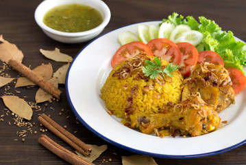 Chicken Biryani on white dish with green sauce (Muslim yellow rice with chicken) on brown wooden background / selective focus ..