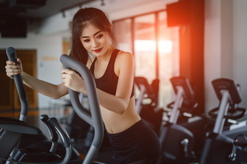 Asian woman Exercise Elliptical cardio running workout at fitness gym taking weight loss with machine aerobic for slim and firm healthy lifestyle in the morning.