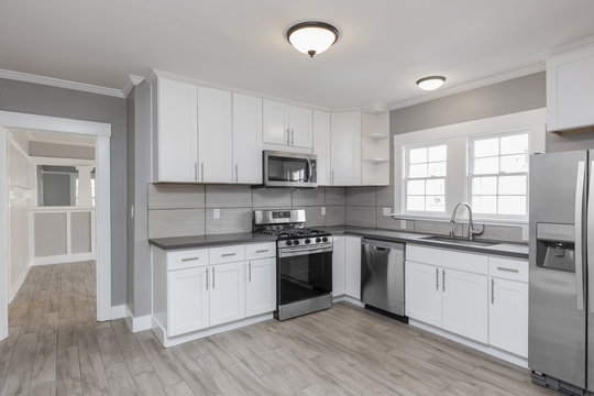 Kitchens in white new, with granite counter-tops, stove and stainless steel refrigerator.