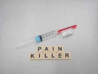 Tan tiles with black capital letters spelling Pain Killer with a syringe and empty glass Fentanyl vial on a stainless steel background.