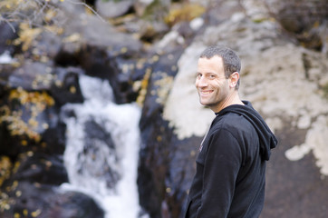 Happy man standing by a small rock waterfall. 