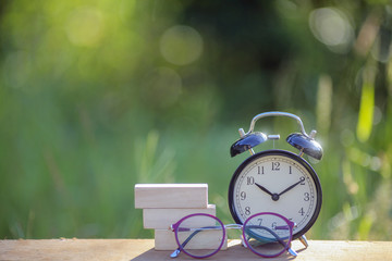 Black alarm clock stacked on wooden bar with shallow DOF green background.