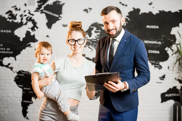 Happy mother and baby boy choosing tour for a summer vacation with male agent at the travel agency office with world map on the background