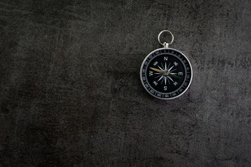 Compass on dark black textured cement with copy space using as direction, travel or adventure journey concept
