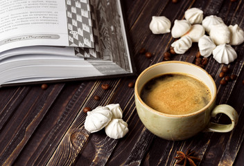 A cup of coffee with meringues and a book on a wooden background
