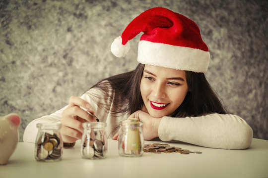 Young woman with red christmas hat looing at piggy bank