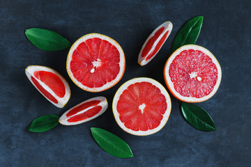 Top view of a vertical composition of slices and halves of grapefruits on a blue background.