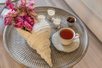 Pink ranunculus in seashell shaped vase and carcade tea in a cup