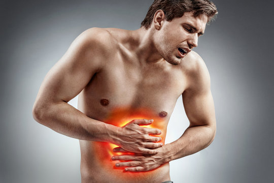 Abdominal pain. Photo of man with naked torso experience irritable bowel syndrome on grey background. Medical concept.