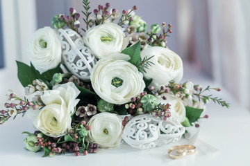 A wedding bouquet of white flowers lies near  to wedding rings for the groom and bride