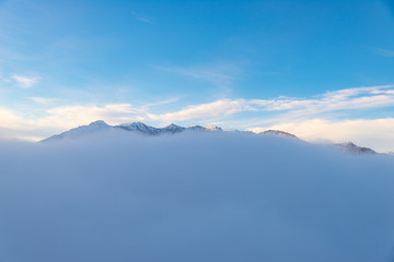 Scenic alpine landscape, clouds on the valley arisign mountain peaks sunset light, winter snow.