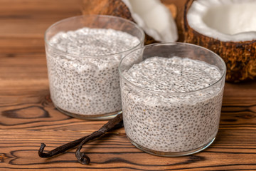 chia pudding in two glass, decorated  vanilla pods and coconuts on wooden background, healthy detox...