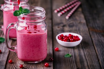 pink smoothie with wild cranberries in mason jar with mint and straw on wooden background