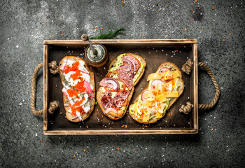 Various sandwiches with seafood, meat and vegetables on an old tray.