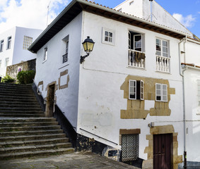Typical old stone house and white walls with balconies and a lantern off on a street of stairs in a village called Pontedeume in La Coruna, Spain. With a blue sky