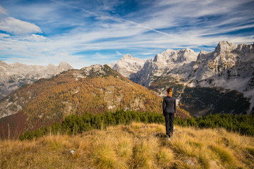 Obraz premium Young female is admiring mount Triglav and Julian alps in autumn colors from a mountain top in Triglav National Park, Slovenia
