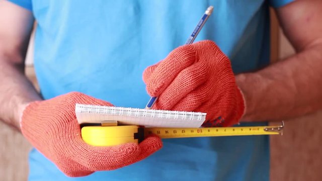 Master in orange gloves holding tape-line and writing