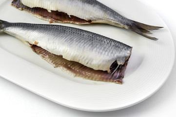 Salted herrings without head on the plate, isolated on white background.