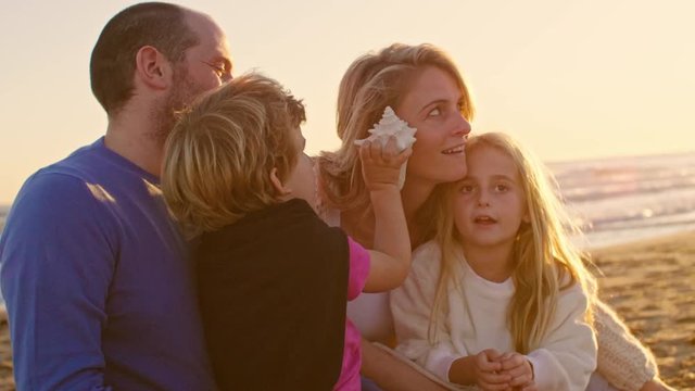 Young family sitting together on beach playing with sea shell