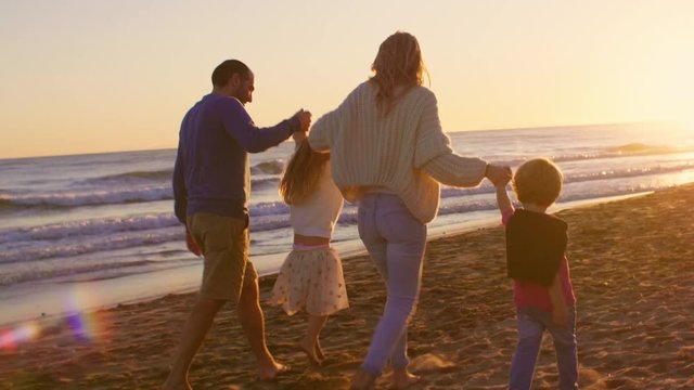 Young family walking and playing on beach in sunset