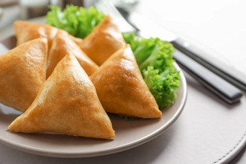 Plate with delicious baked samosas on table, closeup