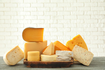 Wooden board with different kinds of delicious cheese on table