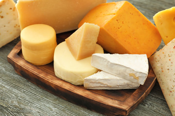 Wooden board with different kinds of delicious cheese on table