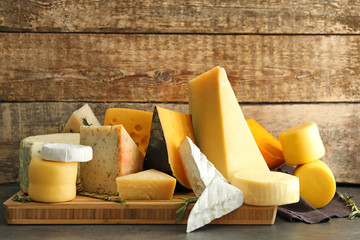 Wooden board with different kinds of delicious cheese on table