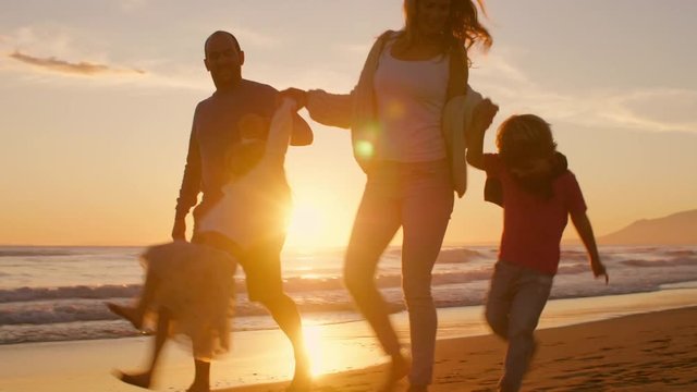 Young family walking and playing on beach with children holding hands in sunset
