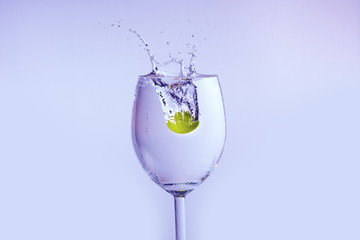 The olive falls into the glass with vodka. Bubbles and splashes appear.