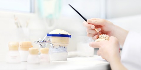 Dental technician hands working with tooth dentures in his laboratory, dental prostheses background concept, web banner
