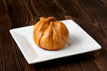 Baked bun on a white plate on a wooden background close-up.