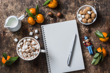 Christmas wooden background with hot chocolate, clean notebook, tangerines, christmas decorations. Free space for text, top view, flat lay